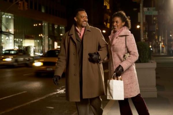 Mature couple standing on pavement holding hands, smiling, night